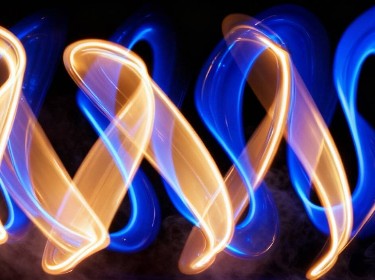 A fire dancer twirls, surrounded by dynamic blue and yellow lights creating a mesmerizing display